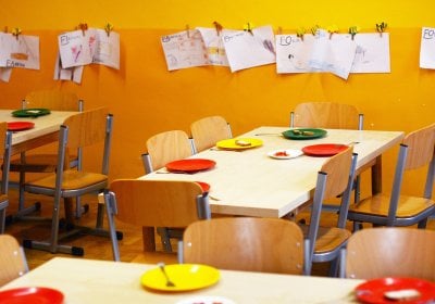 A yellow classroom with children's painting hanging on the walls, tables and chairs with colourful plates