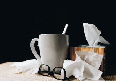 Mug with spoon, discarded tissues and a box of tissues, indicating someone has a cold