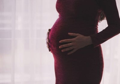 A person who is pregnant holds their stomach, they are wearing a red dress