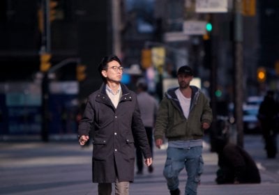 Will wearing a long black coat crosses the road in Toronto, Canada.