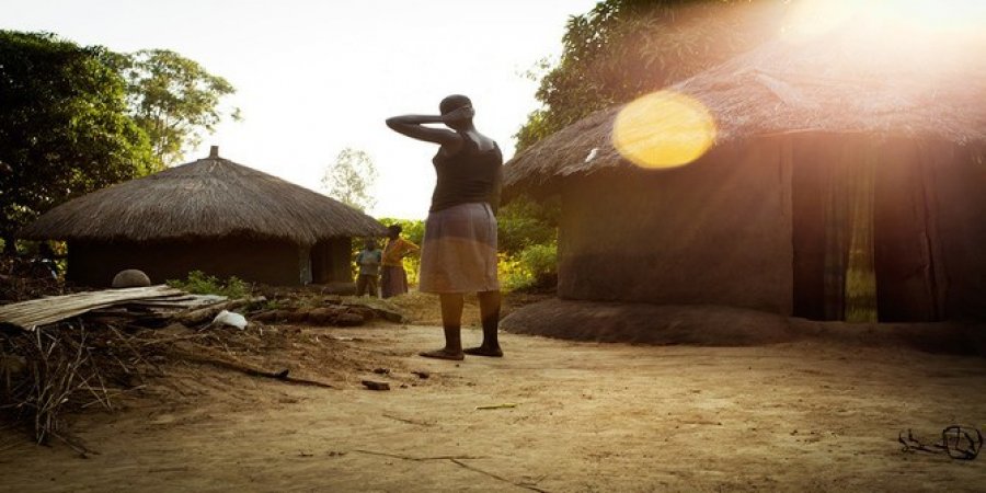 image of woman standing outside huts in uganda 