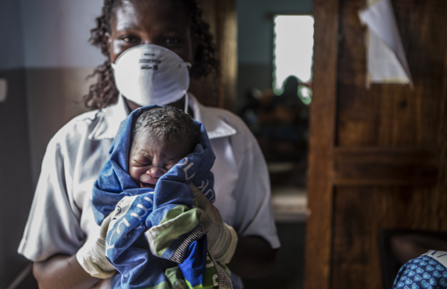 A nurse with face mask holding a newborn baby