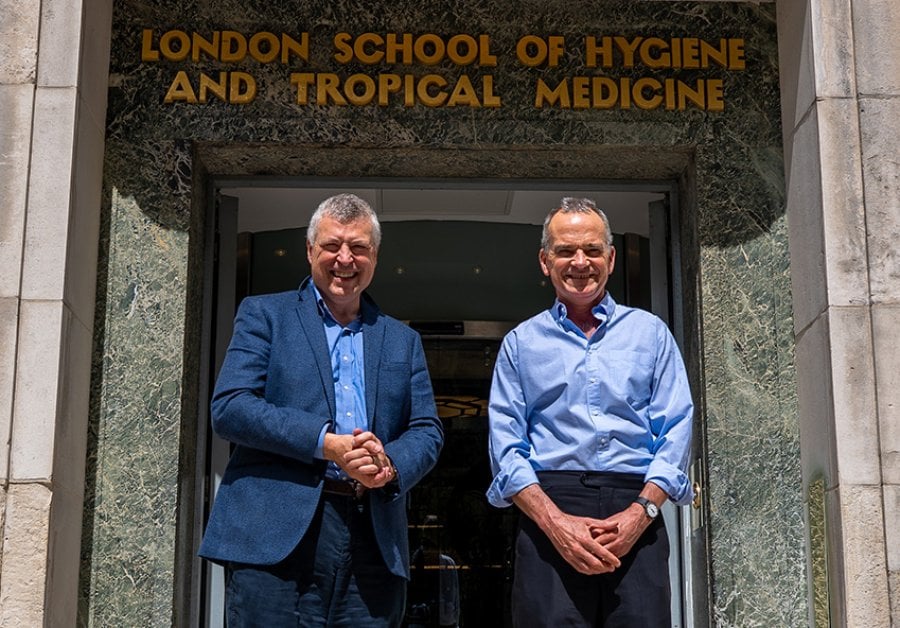 Image of two men in suits and dress shirts standing in front of a doorway, with a frieze overhead reading 'London School of Hygiene and Tropical Medicine'