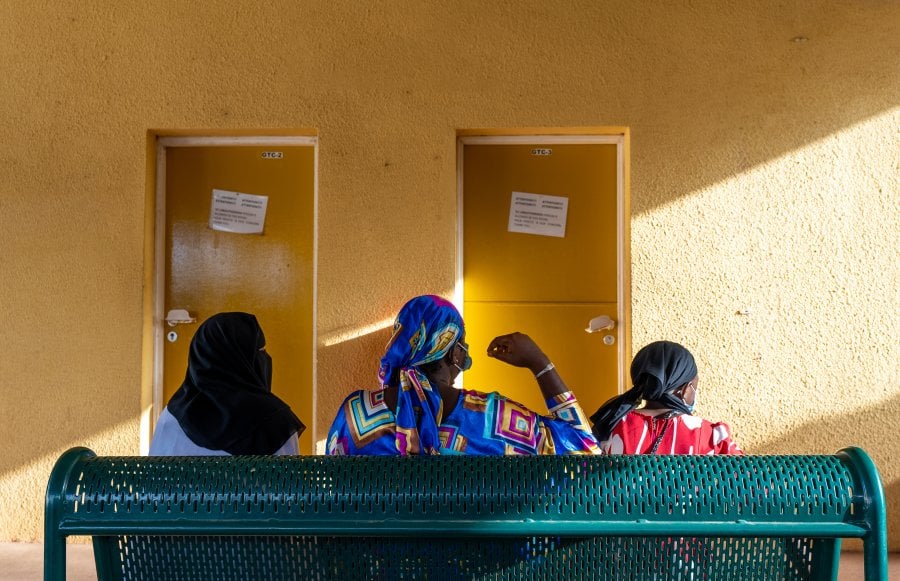 Women seated on a waiting chair with their backs to the camera.