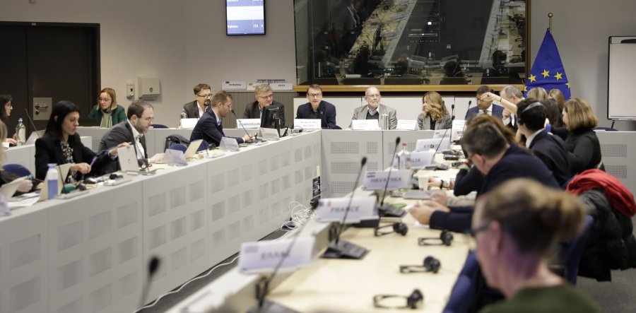 Group of men and women in suits sit around a boardroom table