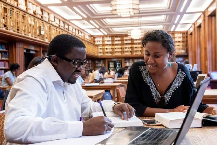Two individuals sitting in the LSHTM library are looking over pieces of work