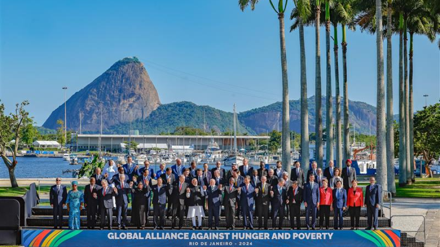 A large group of men and women in suits stand in front of palm trees, sea and mountains