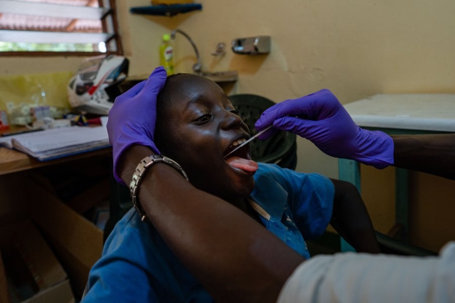 A clinician takes a saliva sample from a young boy, Sibanor, The Gambia.