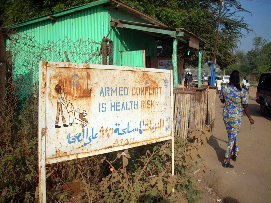 Juba, South Sudan. A sign is posted outside a green tin building and reads “armed conflict is a health risk”. Photo credit: Egbert Sondorp. 