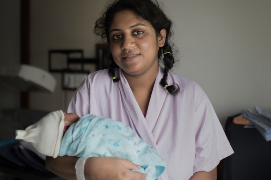 Mum holds her newborn in Bangladesh. Mum wearing pink robe baby in blue blanket.
