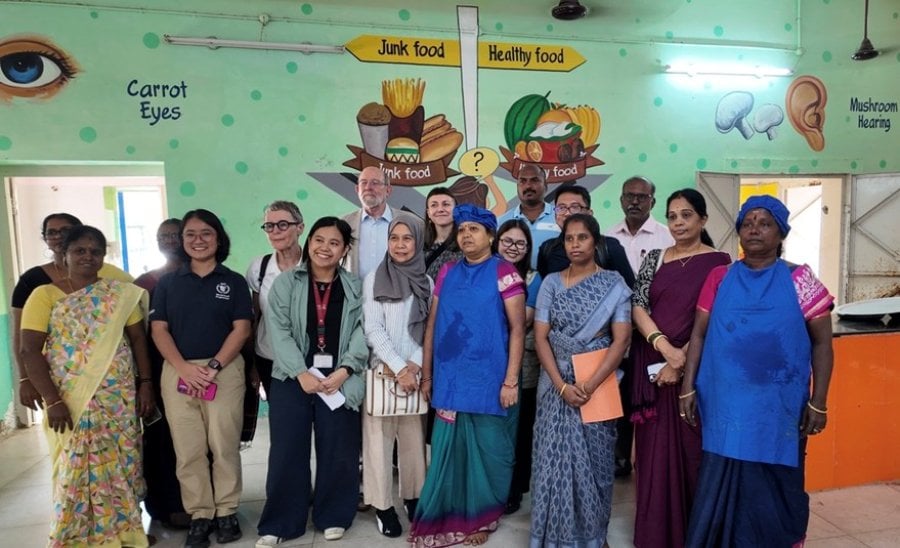A delegation from the Philippines stands next to workers at a school kitchen in India