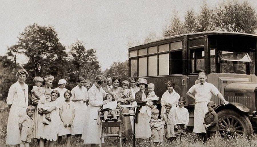 A mobile health unit, parked in a Pennsylvania field: women and their children are shown receiving treatment from the unit's health practitioners. Photograph, 1920/1930? Wellcome Collection