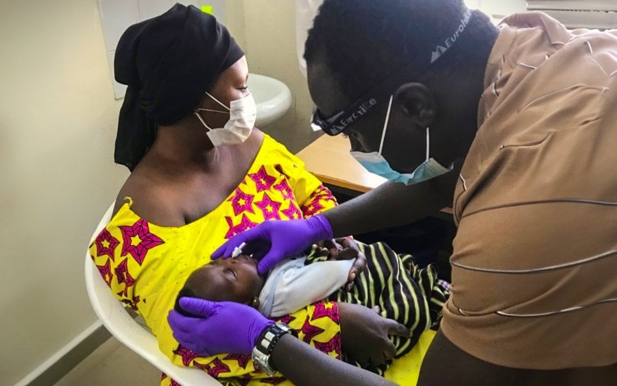 n infant, carried by his mother, being examined by a male nurse.