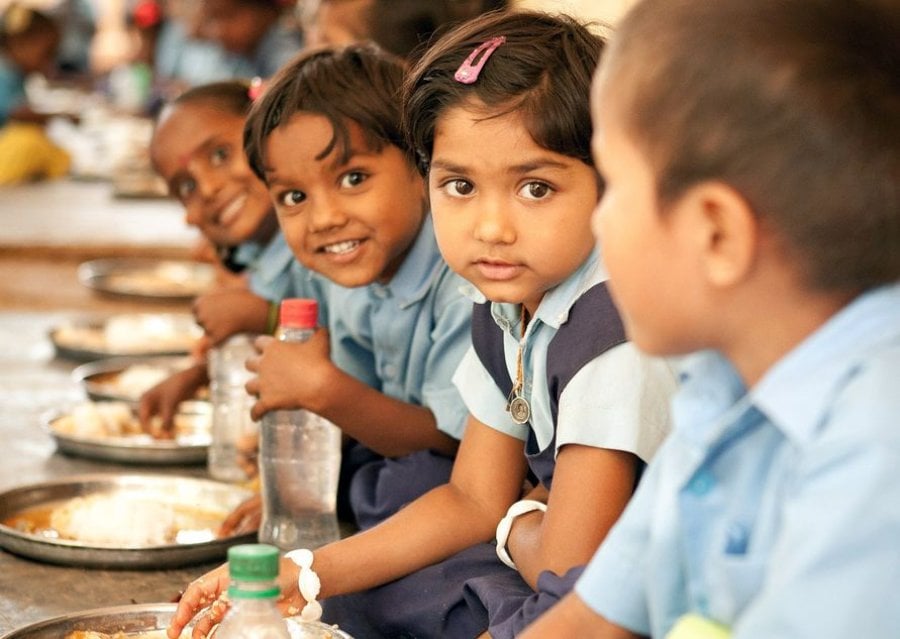 School children in India sit at a bench to eat their midday meal