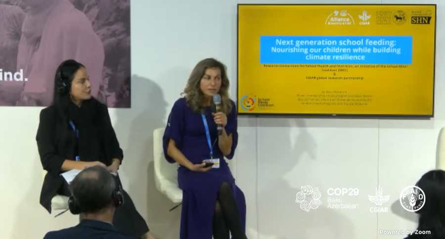 Two women sit on chairs in front of a screen with a presentation title