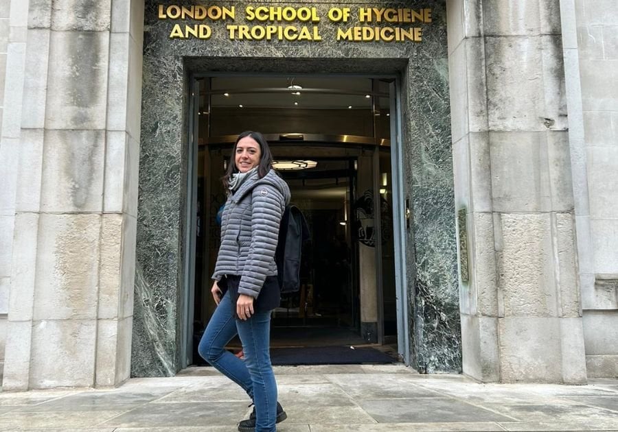 Person stood outside on the steps outside LSHTM entrance wearing a grey coat.