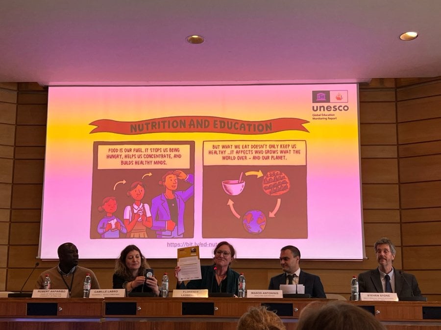 Five speakers in suits sit in front of a screen
