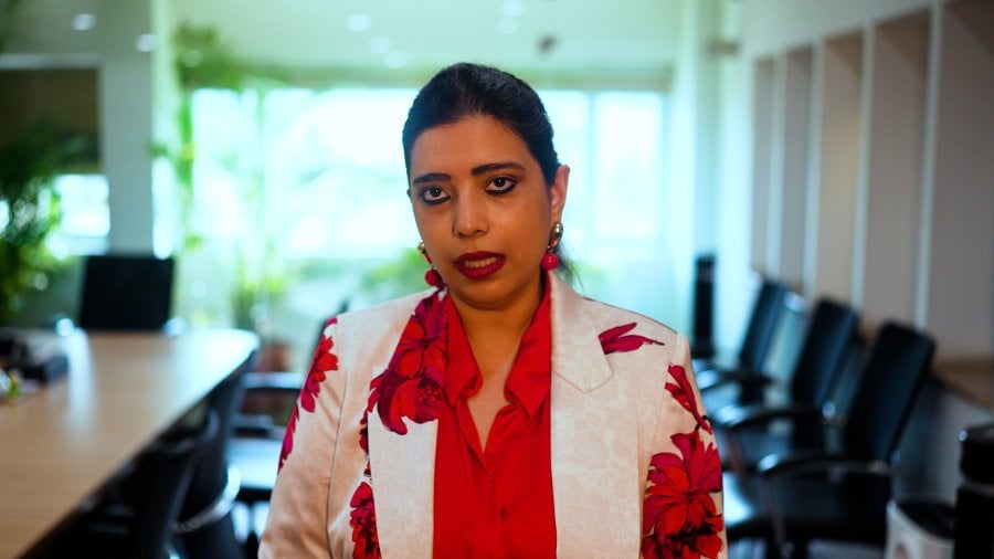 Urvashi sitting in a meeting room wearing a red shirt and white blazer with red flowers.