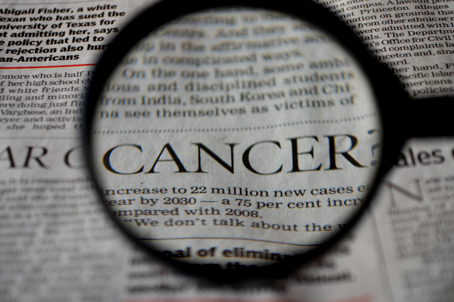 A magnifying glass hovering over a newspaper and the word CANCER is magnified
