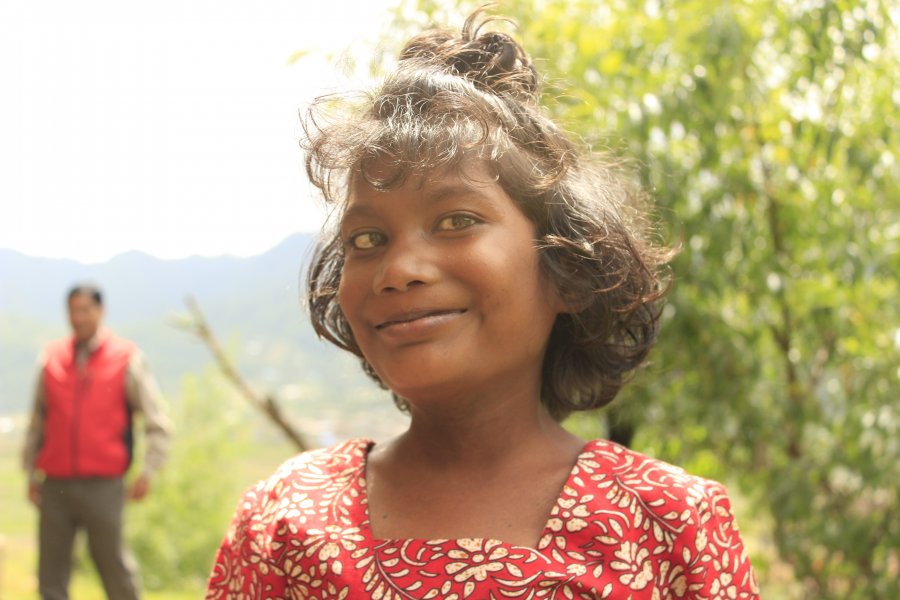 Young girl smiling outside her family home. Photo credit: International Centre for Evidence in Disability