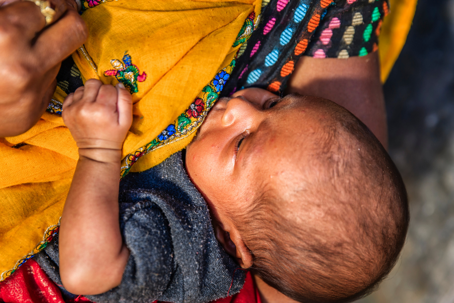 A baby being breastfed by her mother in Jaipur, India. The baby is central in the picture with the mother cropped at the shoulders, but she&#039;s wearing multicoloured clothing and a bright yellow shawl.