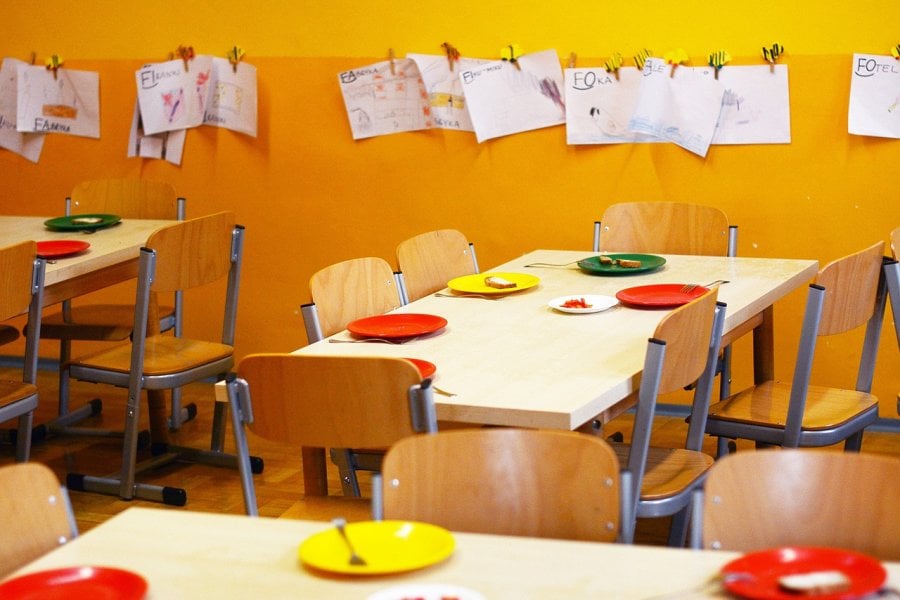 A yellow classroom with children's painting hanging on the walls, tables and chairs with colourful plates