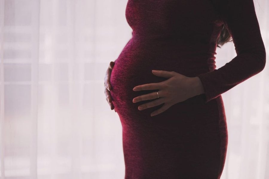 A person who is pregnant holds their stomach, they are wearing a red dress
