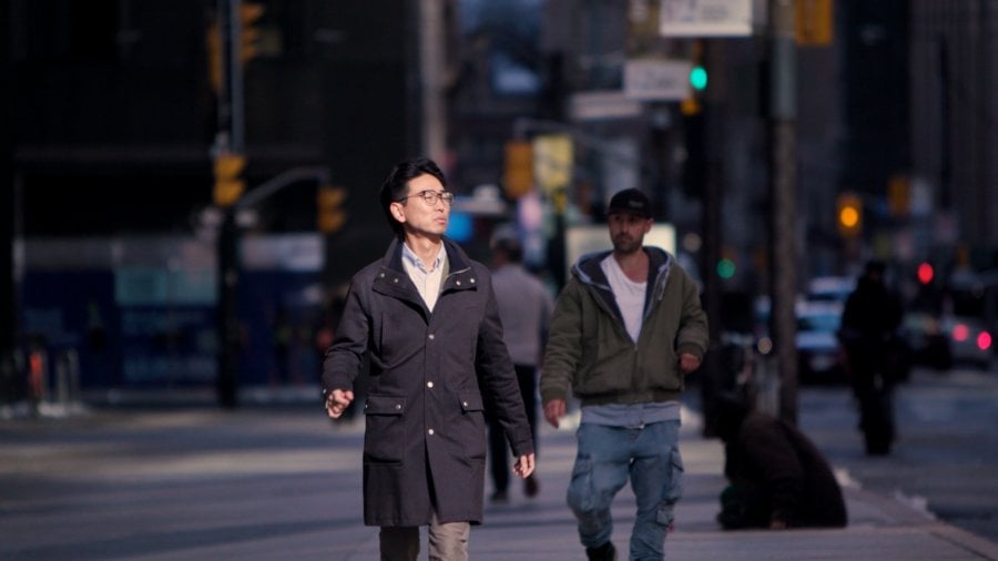 Will wearing a long black coat crosses the road in Toronto, Canada.