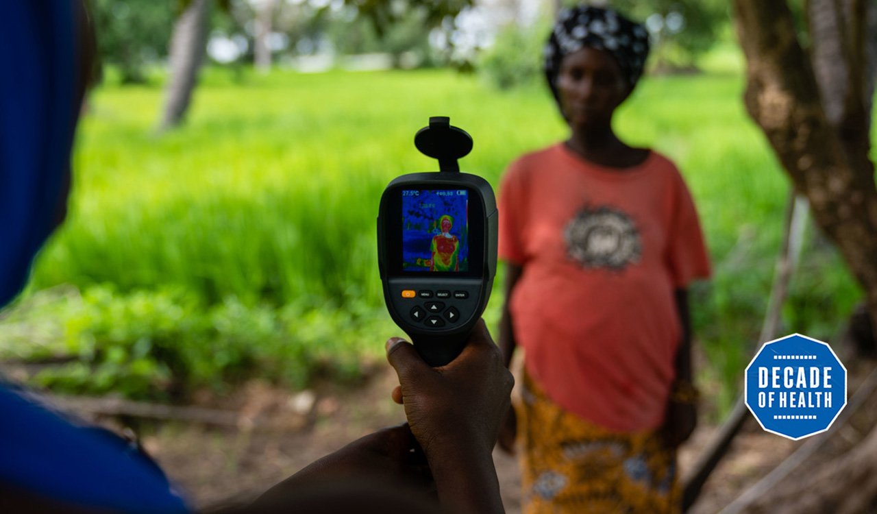 A field worker from MRC Unit The Gambia at LSHTM uses a thermal imaging camera to measure a mother and her unborn baby's temperature in Keneba as part of a study looking at the impact of heat stress on pregnant farmers. Credit: Louis Leeson/LSHTM