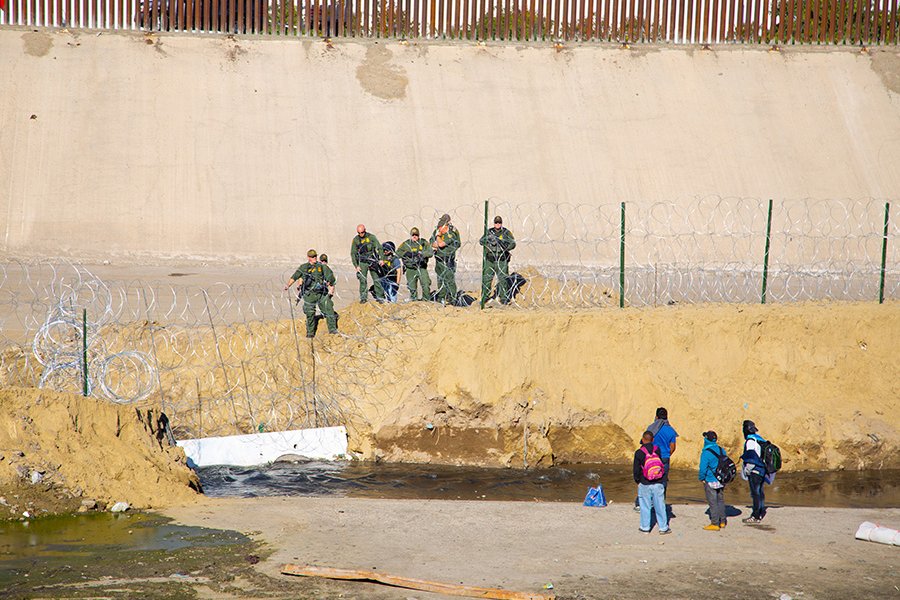 Groups of migrants on opposite side of border fence to enforecement agents. Photo by Humberto Chavez on Unsplash