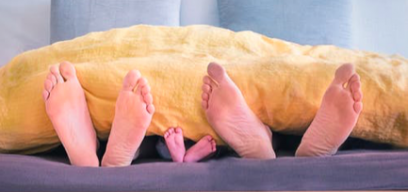 Image of two adult and one child pairs of feet lying on a bed