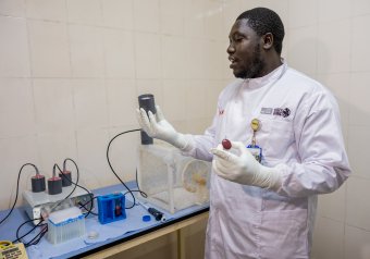 A man wearing a white lab coat in an insectary at MRC Fajara, The Gambia.
