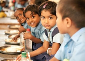 School children in India sit at a bench to eat their midday meal