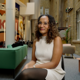 Alumna, Megan, sitting in a social space at LSHTM wearing a cream dress.