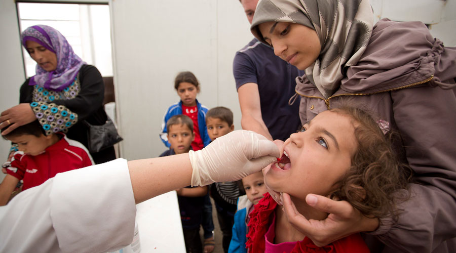 A mother (Syrian refugee) holding her child who is receiving a vaccination