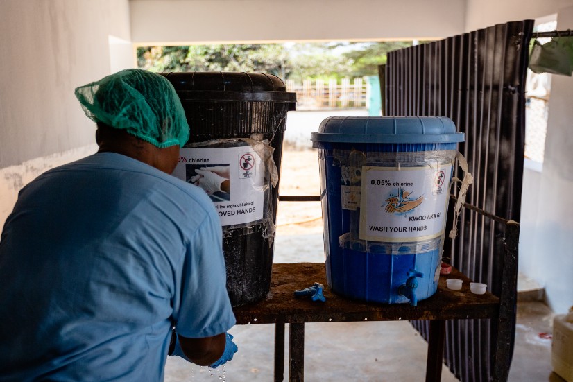 Helathcare worker washing their hands using a chlorine solution in a bucket with nozzle in Nigeria.
